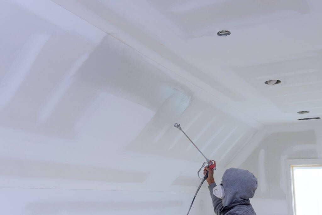 The worker using spray gun with a primer paint walls and ceiling